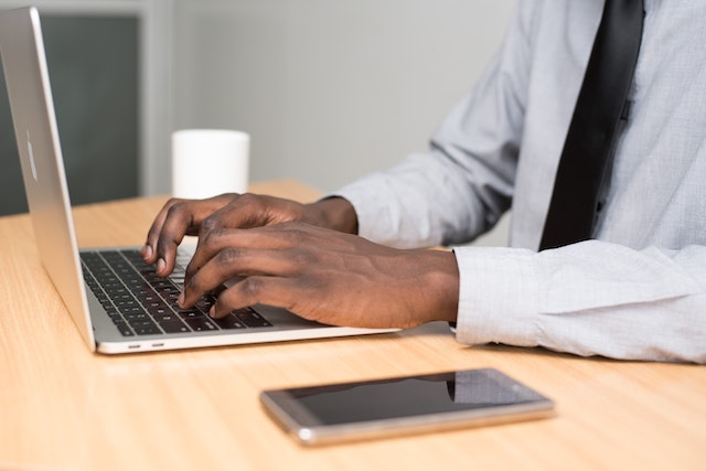 person typing on their laptop with their iPhone next to them on their desk